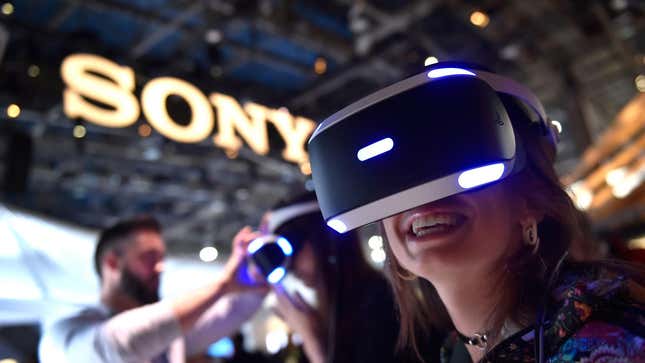 A woman wears a PS VR headset while smiling in front of a Sony sign. 